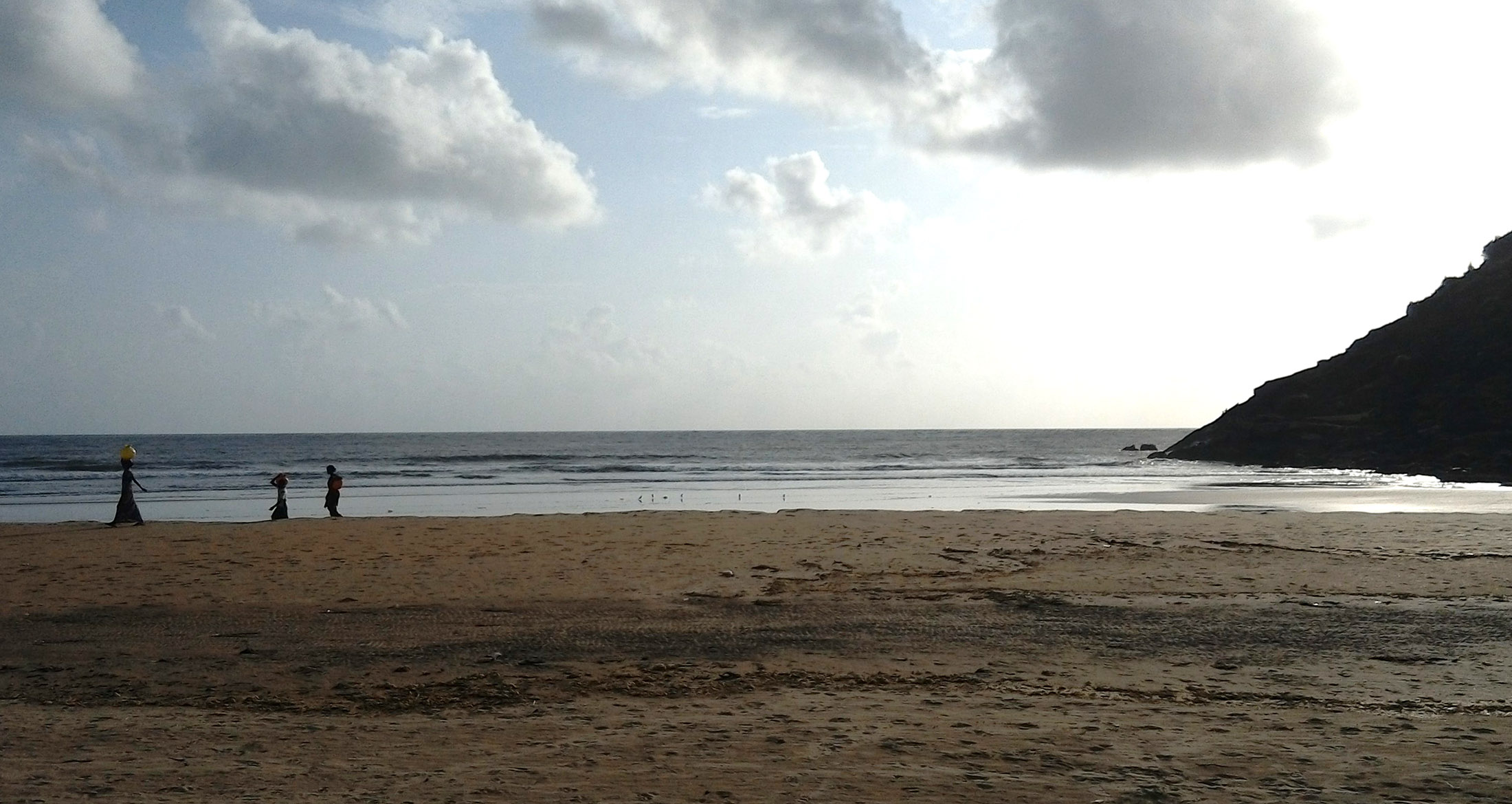Women carrying goods along the shore at dusk, near the estuary